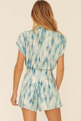 Back view of a woman wearing a blue and white ikat print short sleeve romper with high waisted shorts