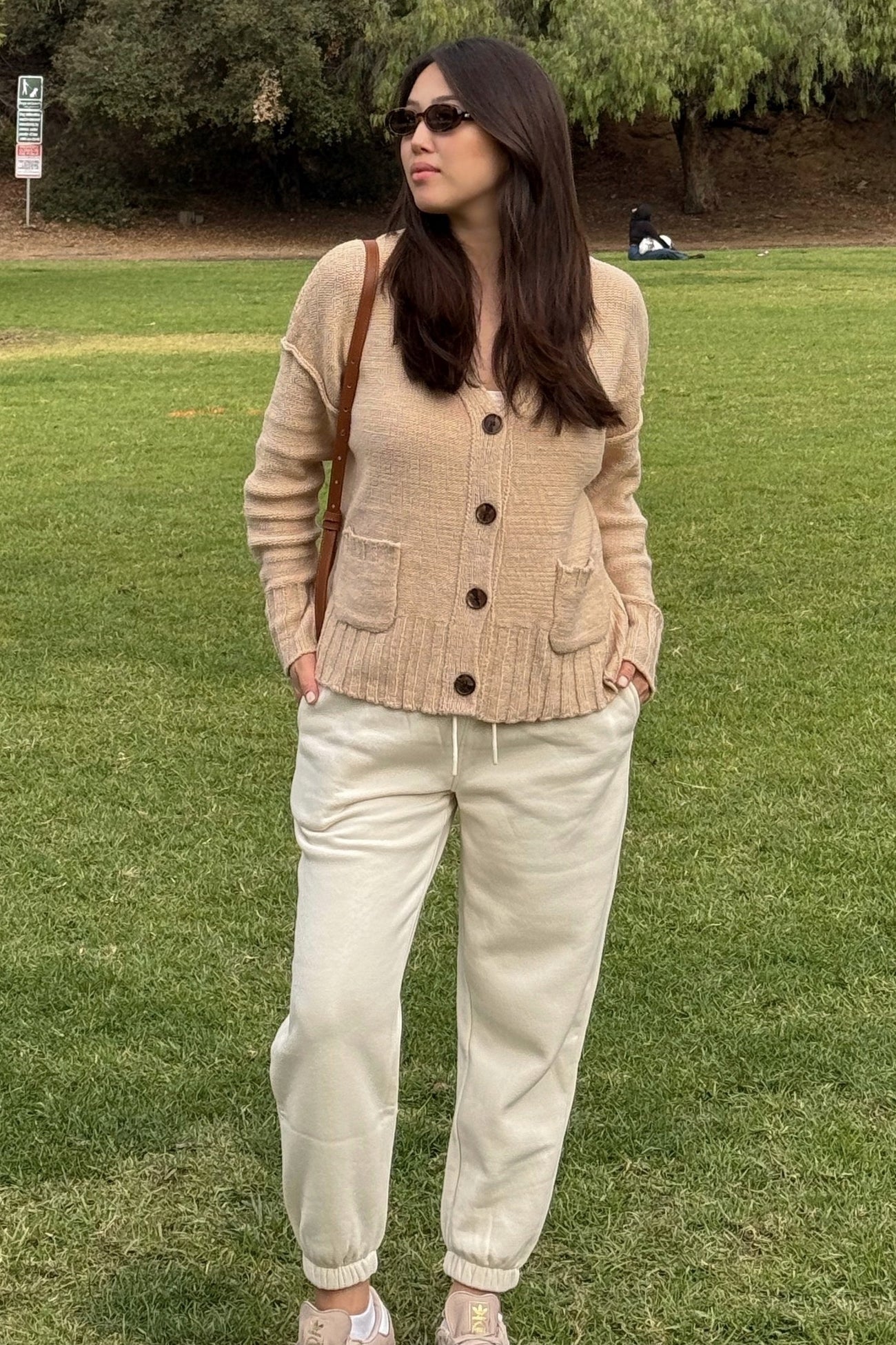woman wearing a beige cardigan with buttons and pockets, paired with cream-colored jogger pants in a park setting
