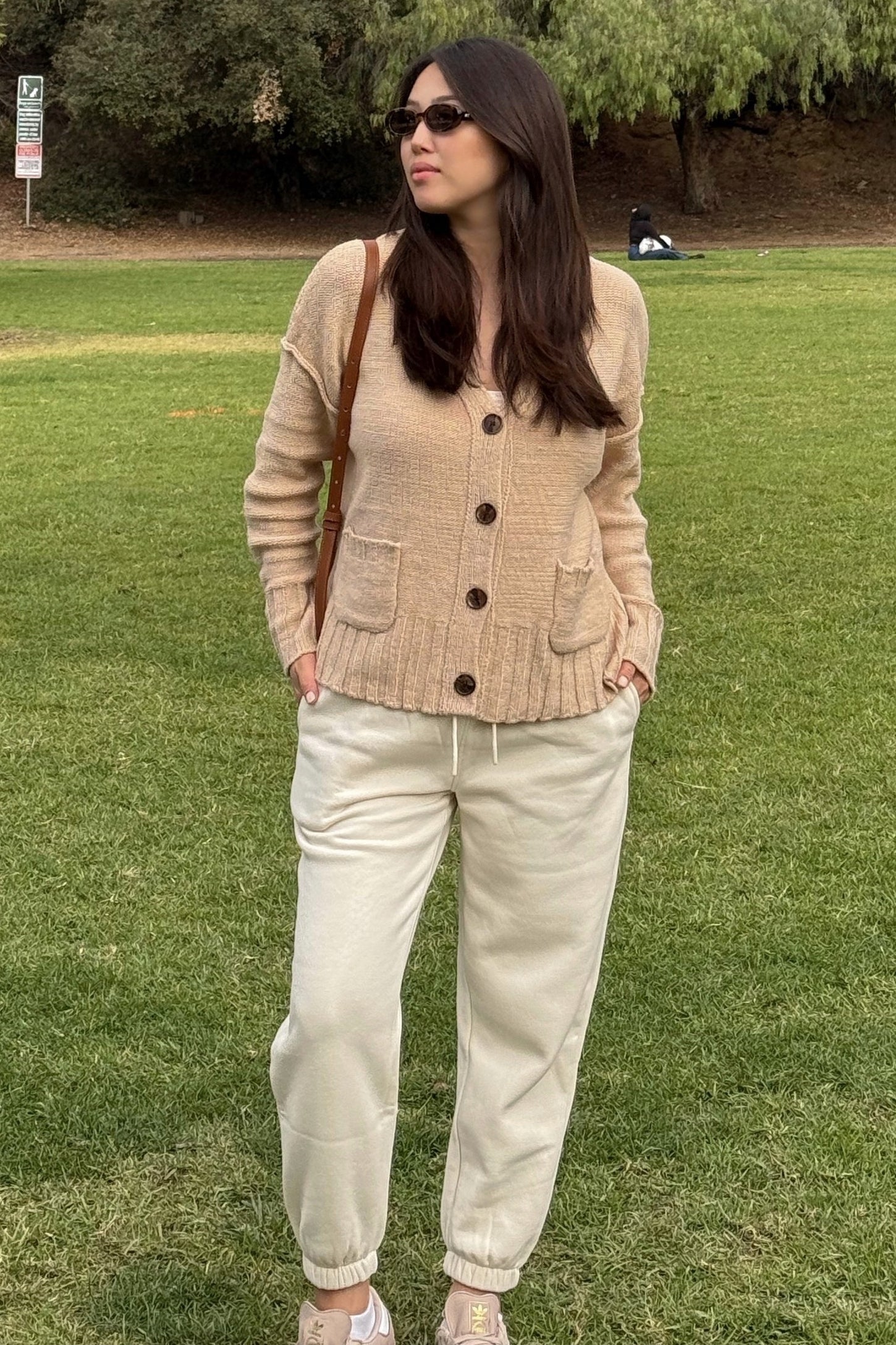 woman wearing a beige cardigan with buttons and pockets, paired with cream-colored jogger pants in a park setting