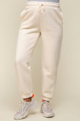 woman wearing cream maternity jogger pants with pockets and elastic cuffs, paired with light sneakers