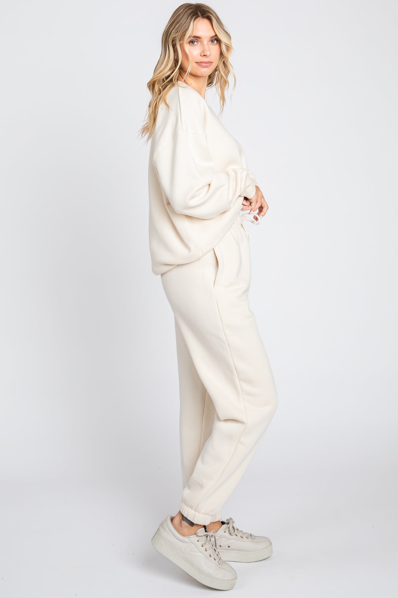 woman wearing a cream oversized sweatshirt and matching jogger pants, styled casually with sneakers