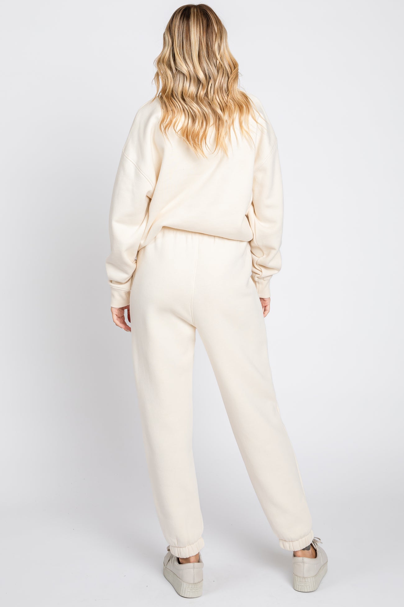 woman wearing a cream oversized sweatshirt and matching jogger pants, viewed from the back