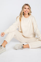 woman wearing a cream oversized sweatshirt and matching joggers, sitting on the floor with a casual pose