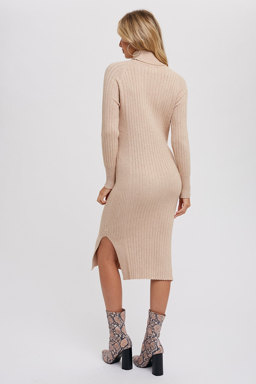 woman wearing a beige ribbed knit midi dress with a high neck and side slit, paired with snake print ankle boots