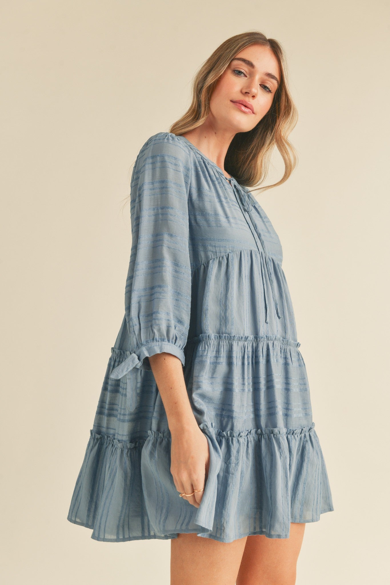 woman wearing a blue tiered mini dress with 3/4 sleeves and a button detail