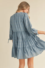 woman wearing a light blue tiered dress with long sleeves and tie details on the sleeves