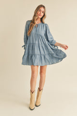 woman wearing a light blue tiered mini dress with tied sleeves and a round neckline, styled with cowgirl boots