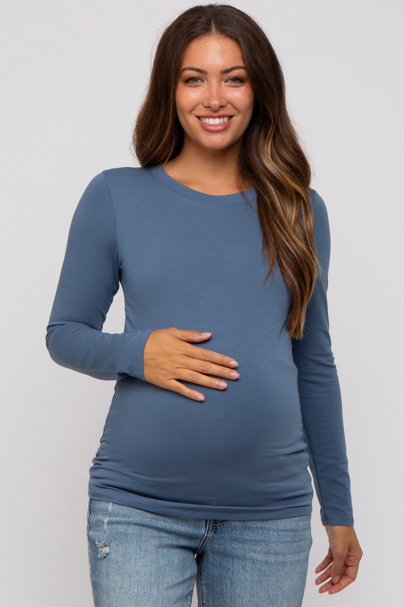 woman wearing a blue long sleeve maternity top and showing her baby bump while smiling