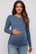 woman wearing a blue long sleeve maternity top and showing her baby bump while smiling