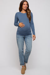 woman wearing a blue long sleeve maternity top and distressed jeans, showing her baby bump while smiling