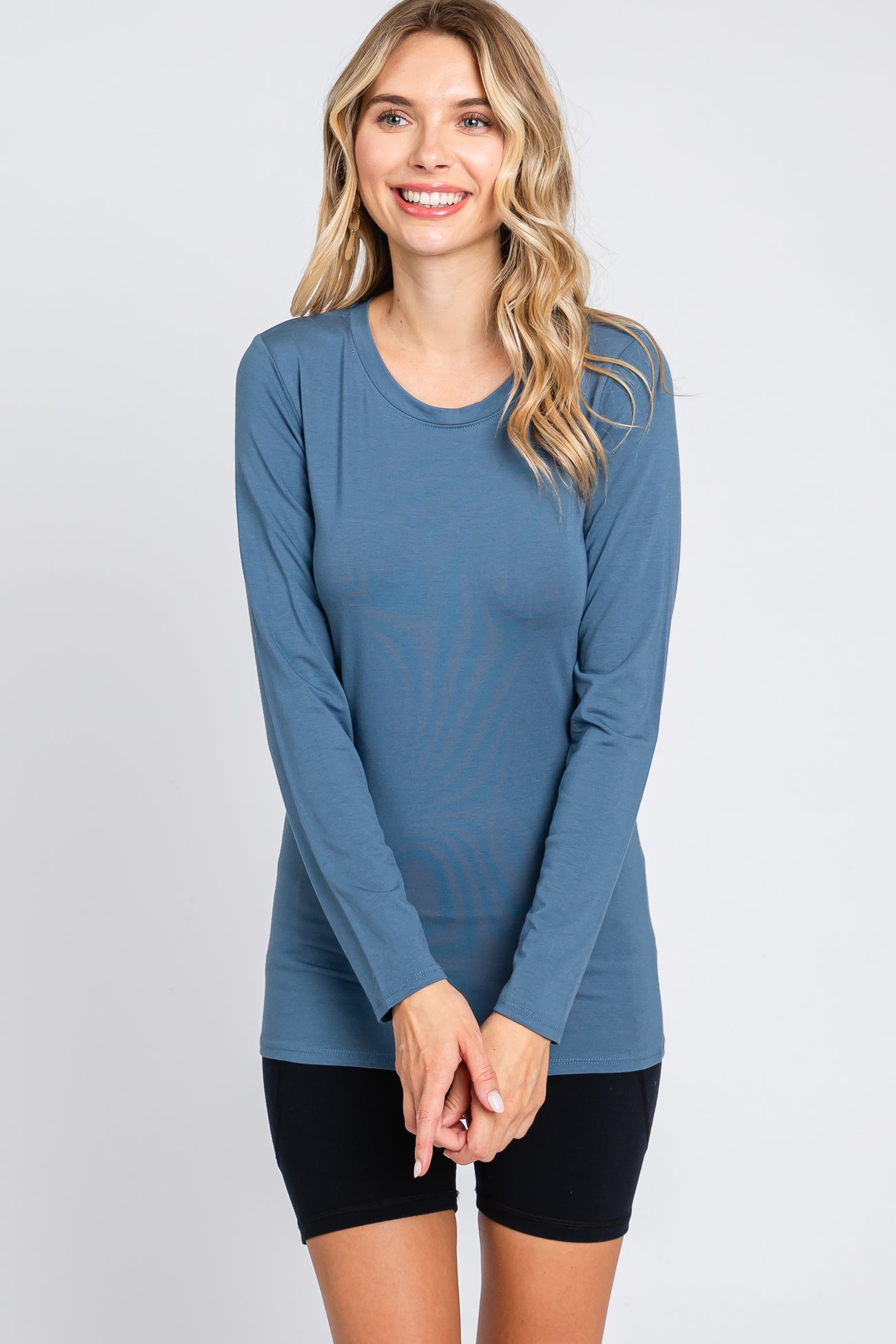 woman wearing a blue long sleeve top with a round neck and smiles while standing against a plain background