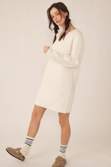 woman wearing a cream knitted sweater dress with long sleeves and standing in a playful pose