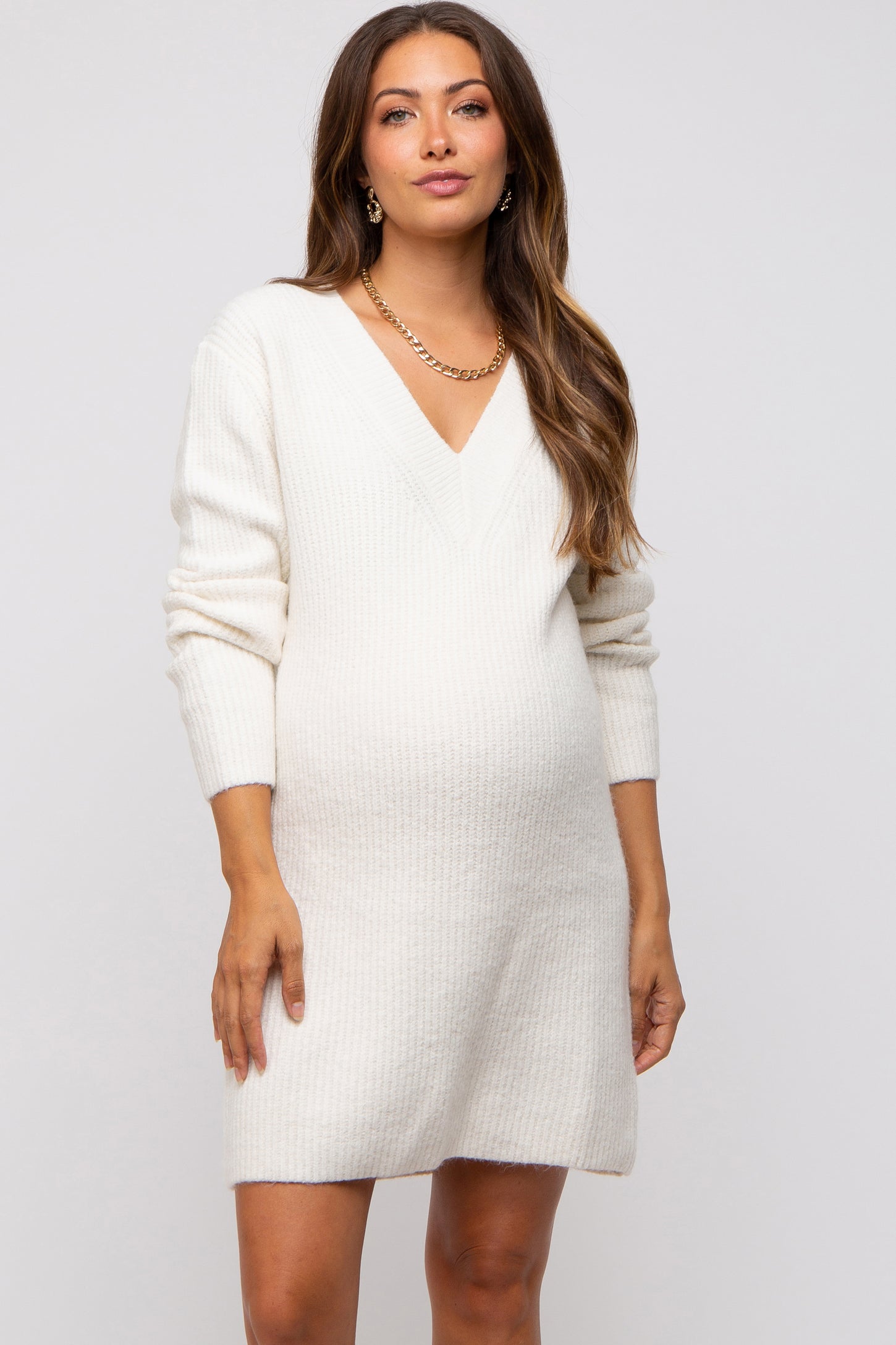woman wearing a cream v-neck knit maternity dress and showing her baby bump