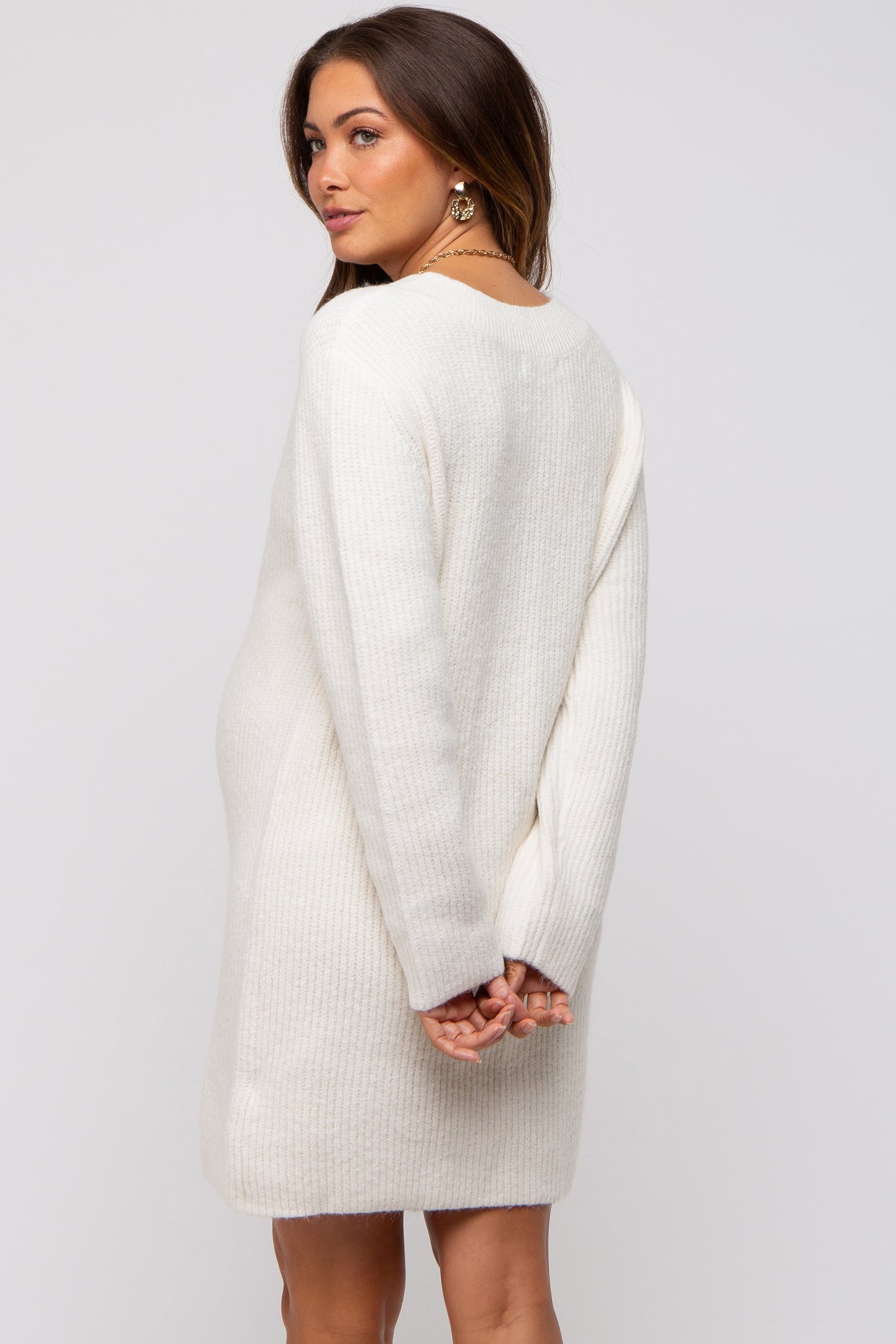 woman wearing a cream-colored maternity sweater dress, showing a baby bump from the back