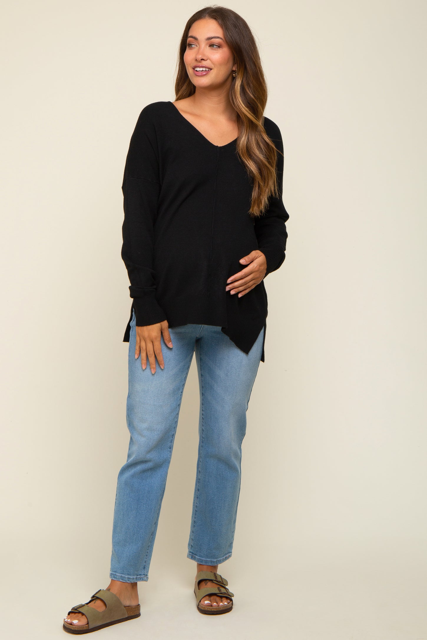 woman wearing a black v-neck maternity sweater and blue jeans, smiling and holding her baby bump