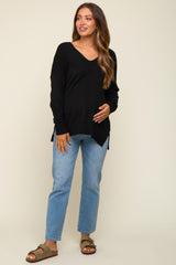 woman wearing a black v-neck maternity sweater and blue jeans, smiling and holding her baby bump