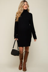 woman wearing a black ribbed maternity sweater dress with a turtleneck and knee-high brown boots, holding a black handbag