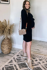 woman wearing a black ribbed maternity dress and holding her baby bump, accessorized with a patterned handbag and ankle boots