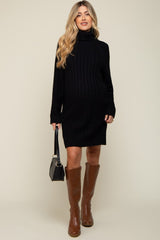 woman wearing a black ribbed maternity sweater dress with a turtleneck and knee-high brown boots, showcasing her baby bump