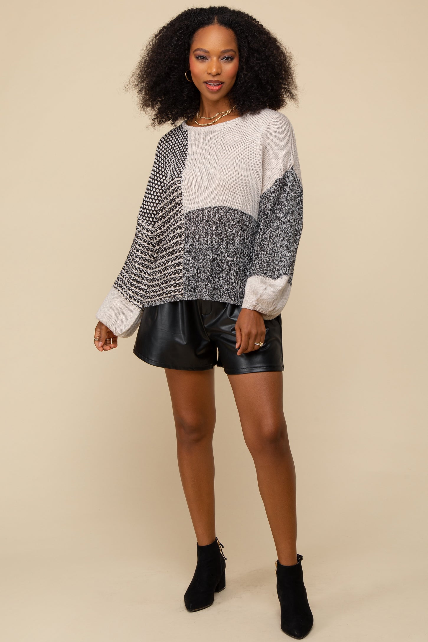 woman wearing oversized patchwork knit sweater and black leather shorts with ankle boots