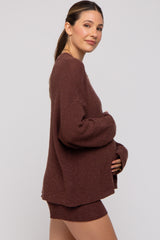 woman wearing a chocolate brown maternity sweater and matching shorts, gently cradling her baby bump