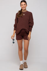 woman wearing a maroon maternity sweater and matching shorts, showcasing her baby bump, styled with sunglasses and light shoes