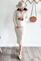 woman wearing a cream ribbed midi maternity dress with buttons, holding her baby bump, and wearing a wide-brimmed hat