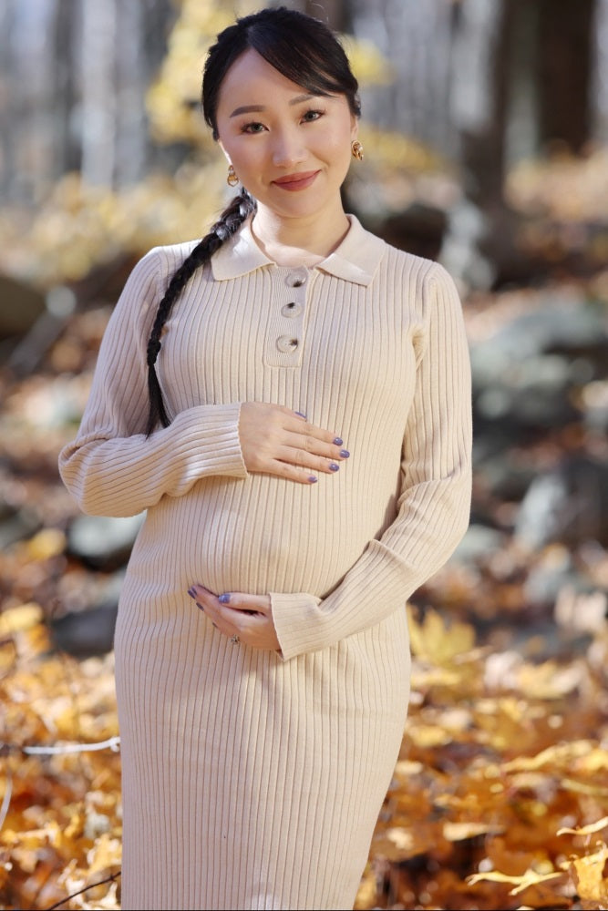 woman wearing a beige ribbed maternity sweater dress and holding her baby bump in an autumn outdoor setting