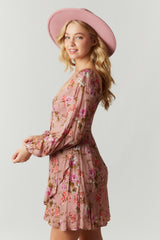 Woman in a pink floral long sleeve mini dress and matching wide brim hat against a white background