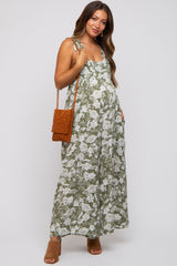 woman wearing a floral green maternity maxi dress with adjustable straps and holding a tan handbag
