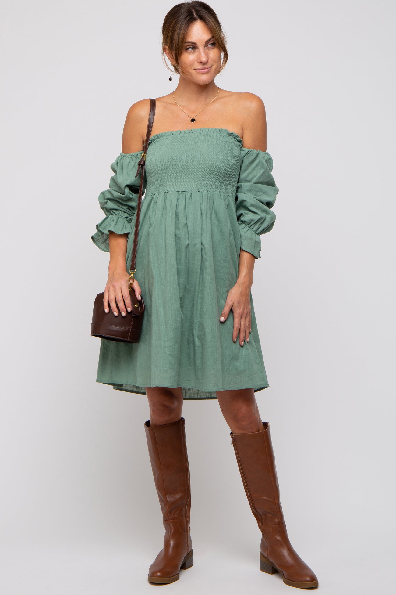 woman wearing a green off-the-shoulder smocked dress with puff sleeves and brown knee-high boots