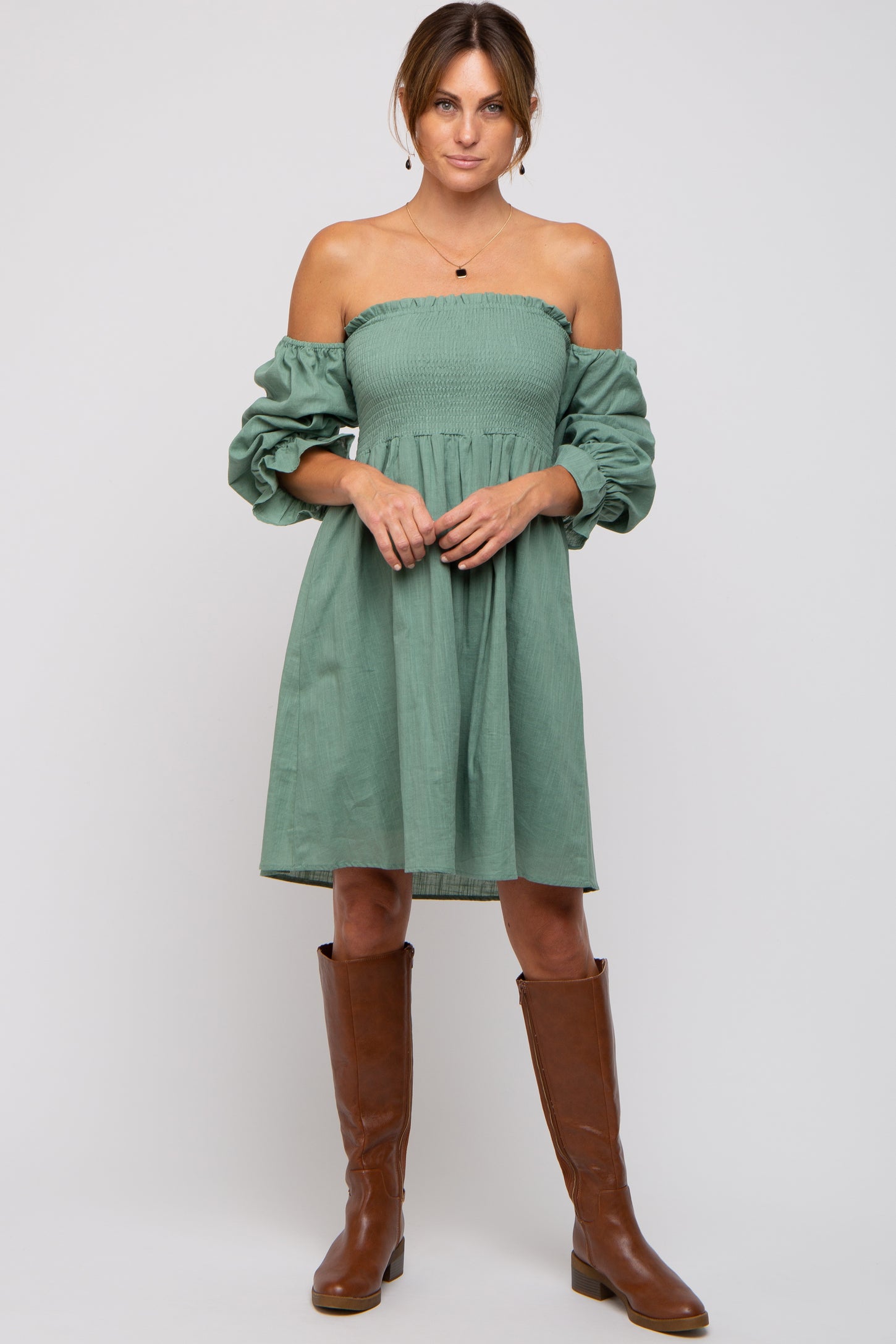woman wearing a green off-the-shoulder dress with puffed sleeves and knee-high brown boots