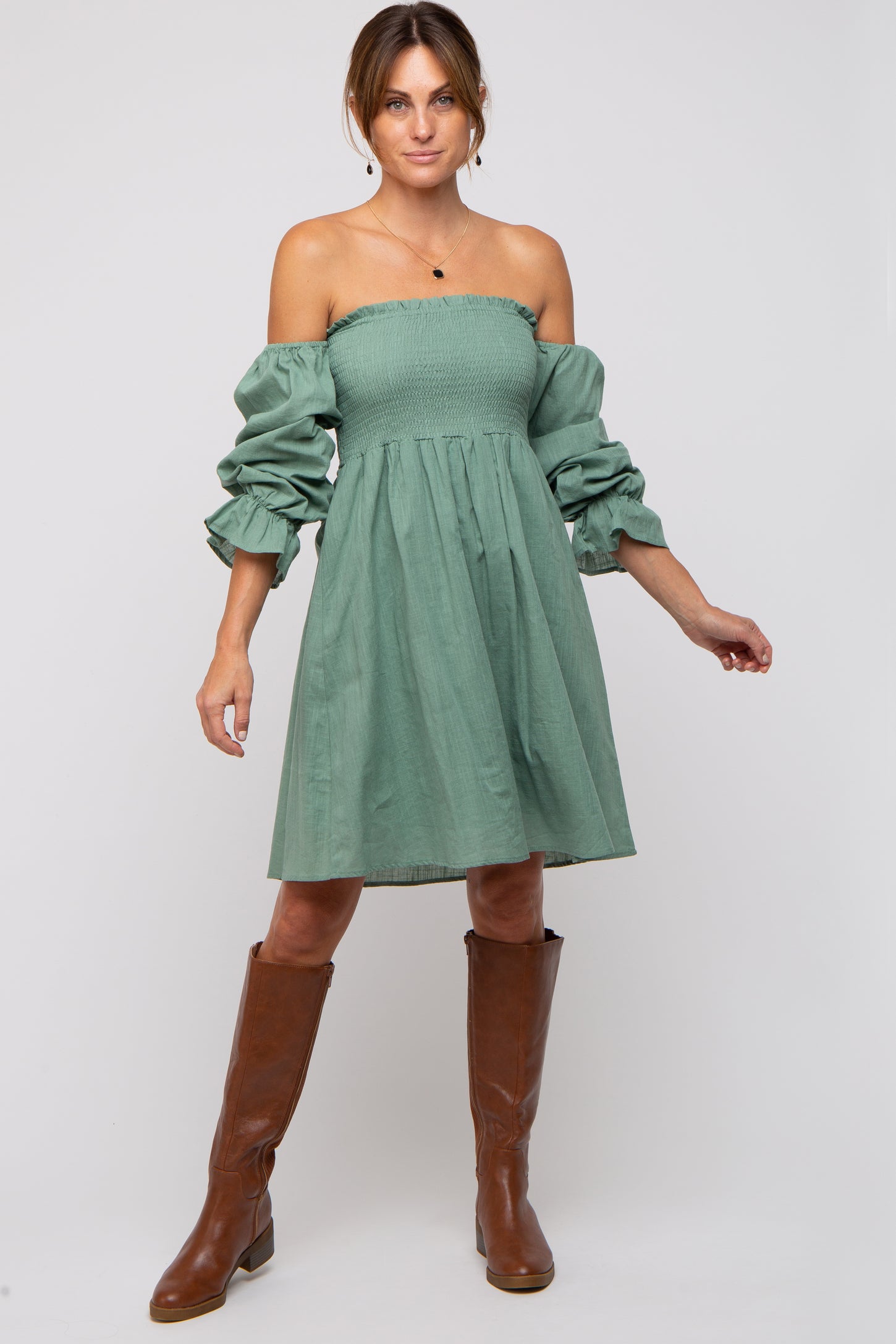 woman wearing a green off-shoulder dress with puff sleeves and a fitted bodice, paired with brown knee-high boots