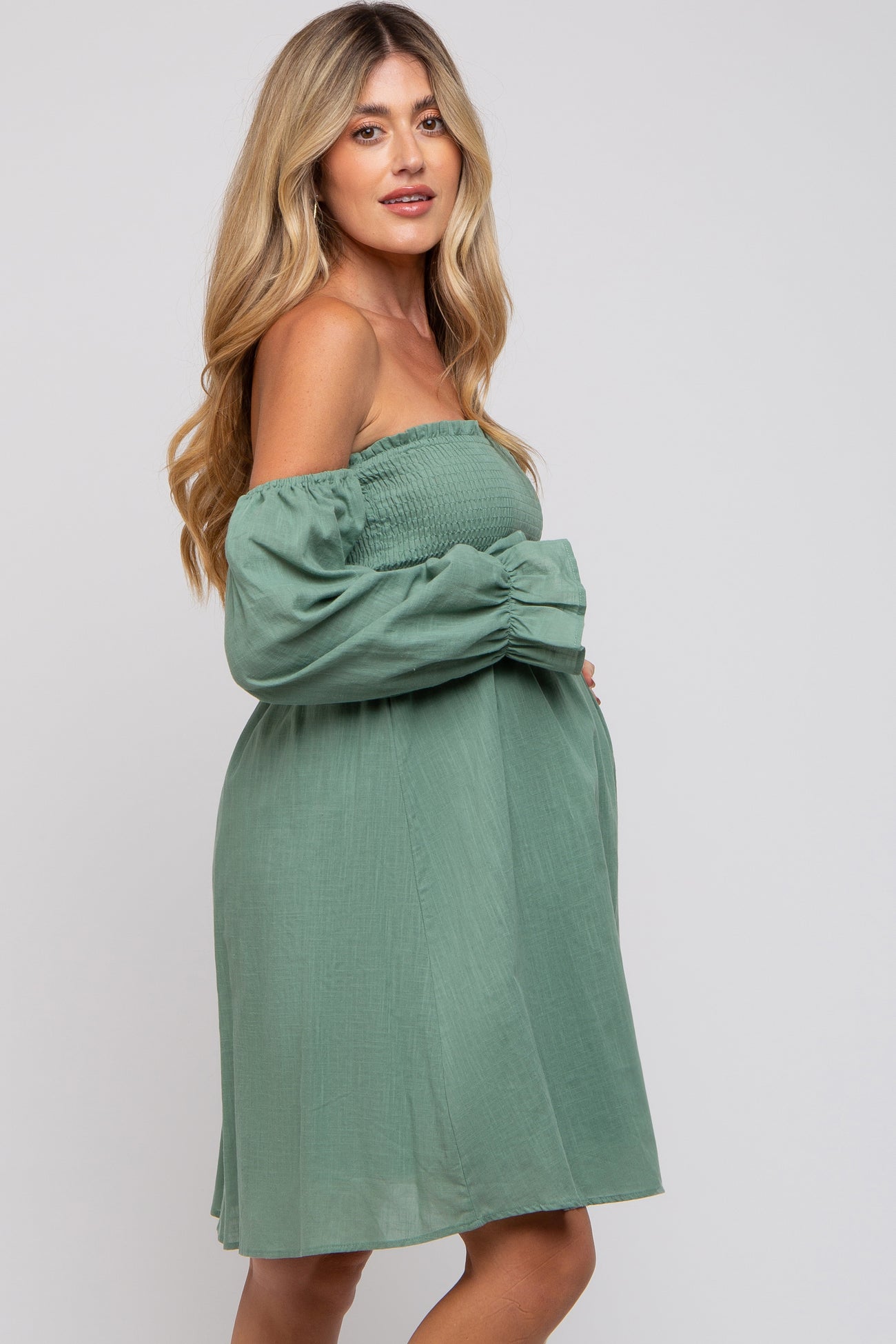 woman wearing a green off-the-shoulder maternity dress with a smocked bodice and a visible baby bump