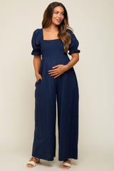 woman wearing a navy blue smocked maternity jumpsuit with puff sleeves, holding her baby bump