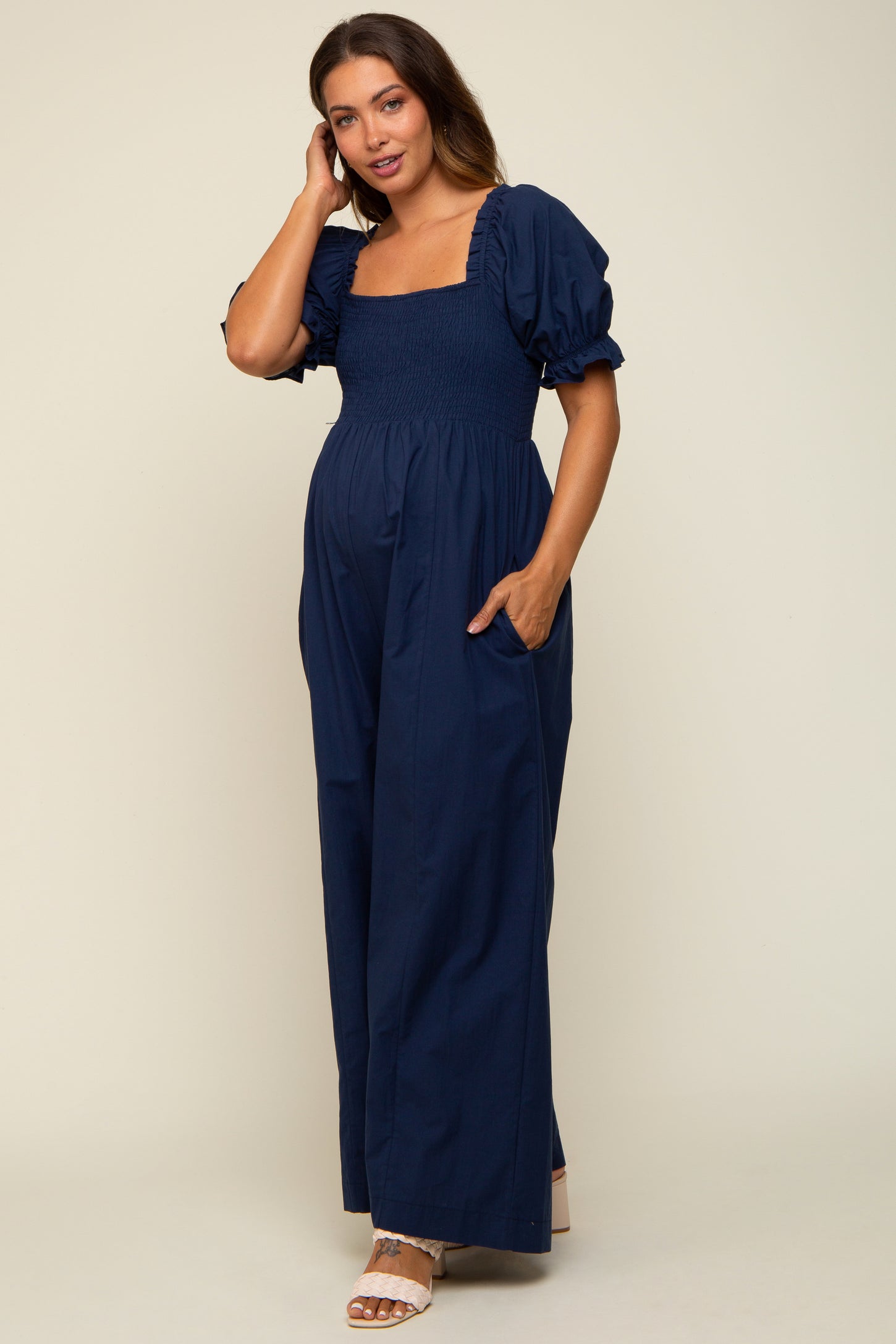 woman wearing a navy maternity jumpsuit with puff sleeves and a square neckline, showing her baby bump