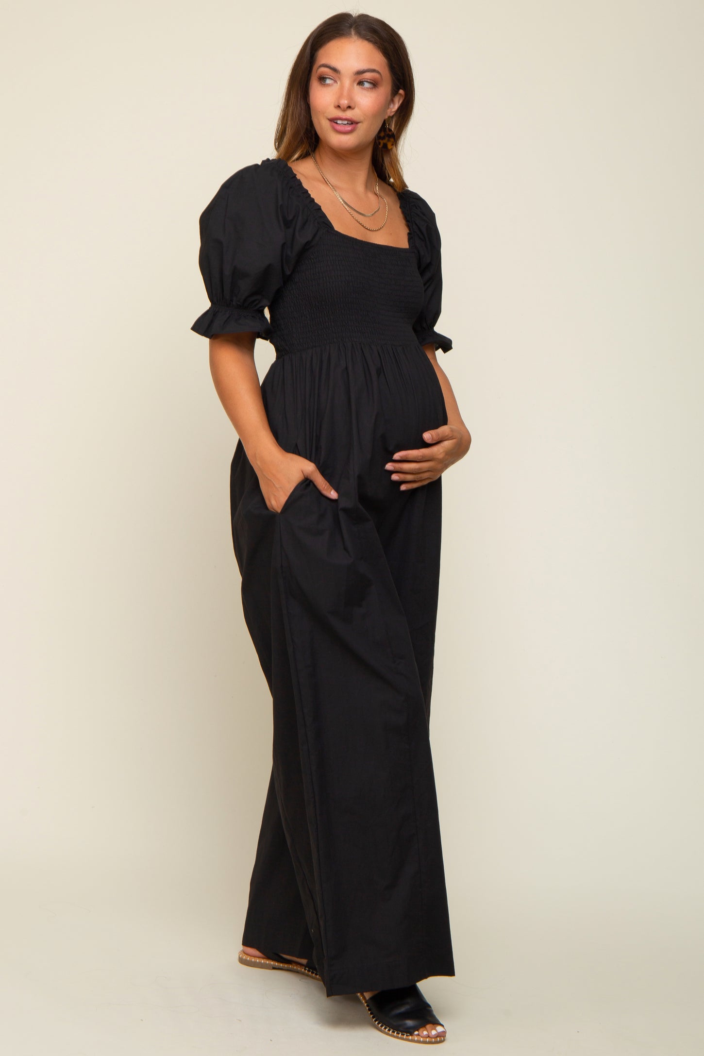 woman wearing a black maternity dress with short puff sleeves and pockets, holding her baby bump