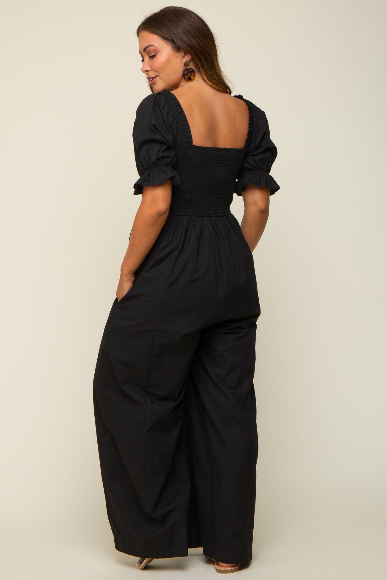 woman wearing a black maternity jumpsuit with puff sleeves and a smocked back, featuring a wide-leg silhouette