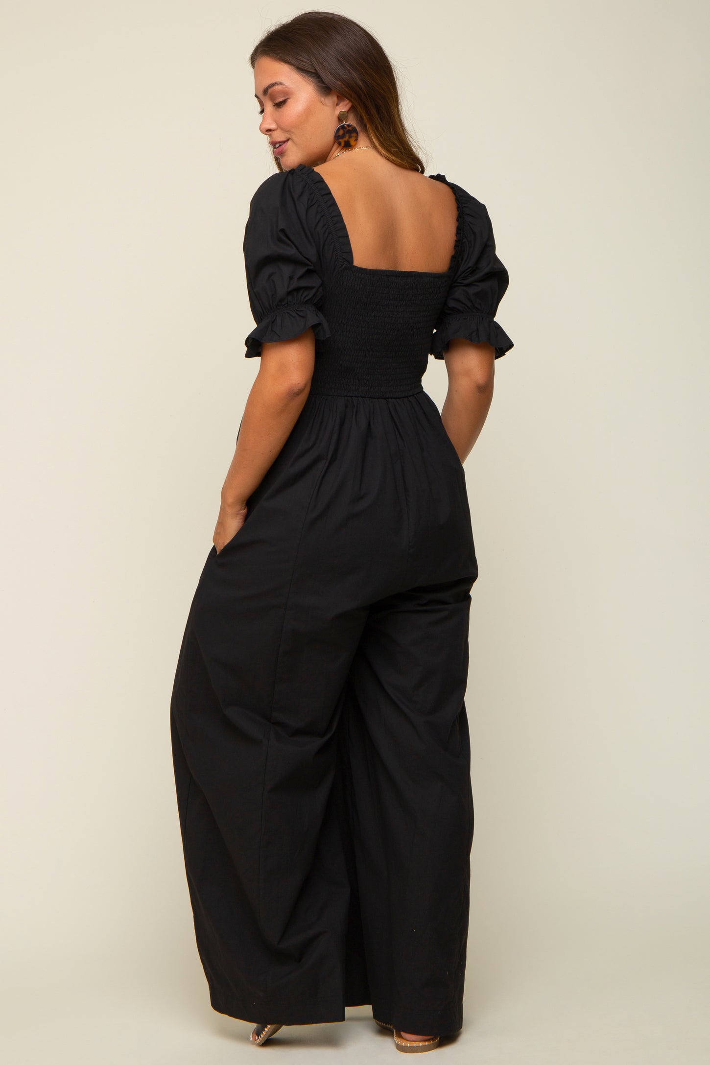 woman wearing a black maternity jumpsuit with puff sleeves and a smocked back, featuring a wide-leg silhouette