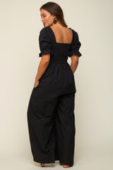 woman wearing a black maternity jumpsuit with puff sleeves and a smocked back, featuring a wide-leg silhouette
