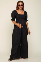 woman wearing a black maternity jumpsuit with puff sleeves, holding her baby bump