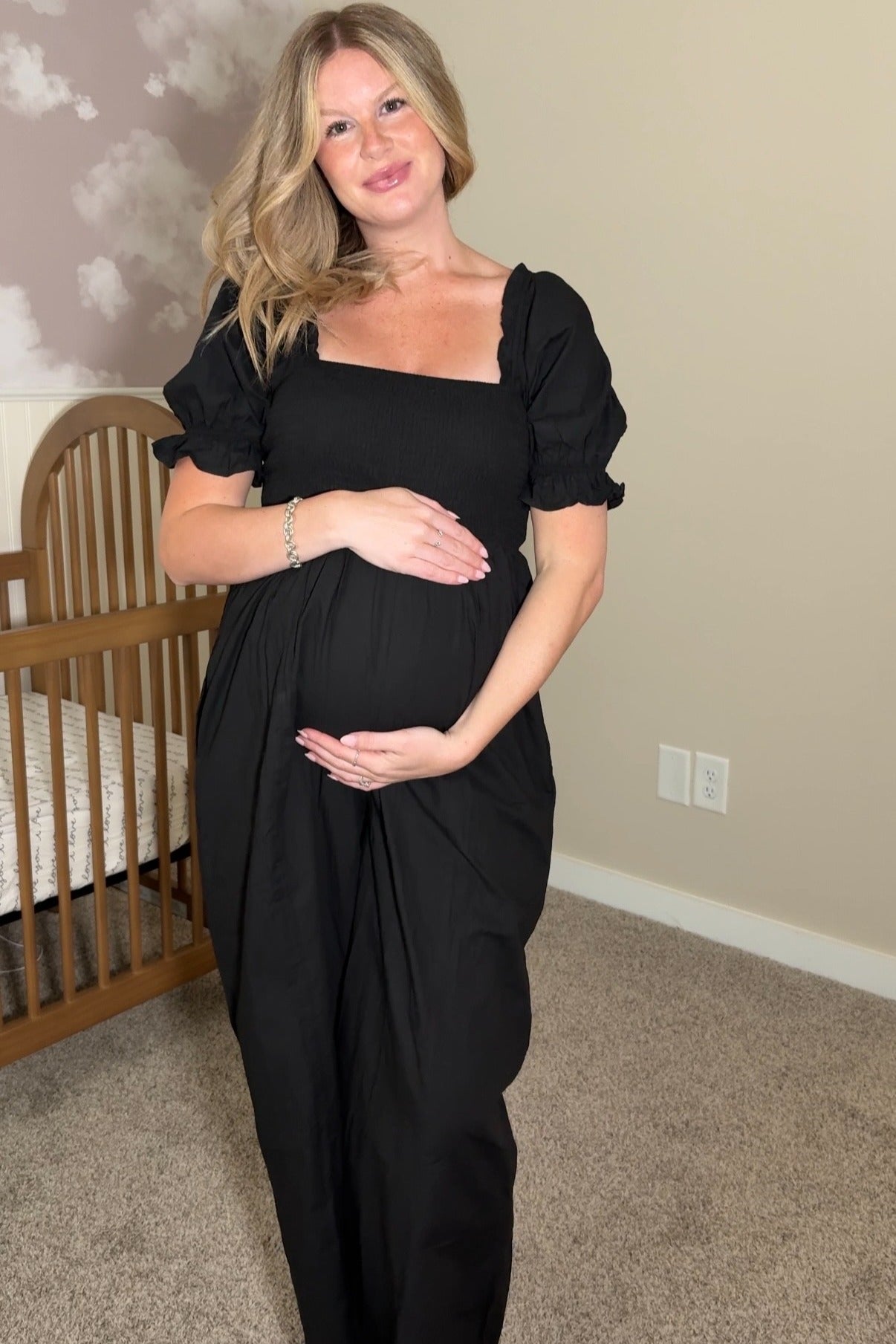 woman wearing a black maternity dress with puff sleeves, holding her baby bump in a nursery setting