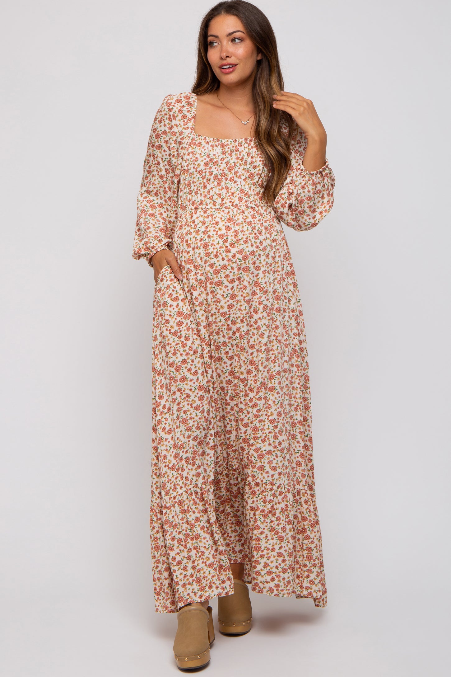woman wearing a floral maxi dress with long sleeves and pockets, showcasing her baby bump in this maternity wear