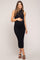 woman wearing a black ribbed maternity dress with a sleeveless design, lightly holding her baby bump