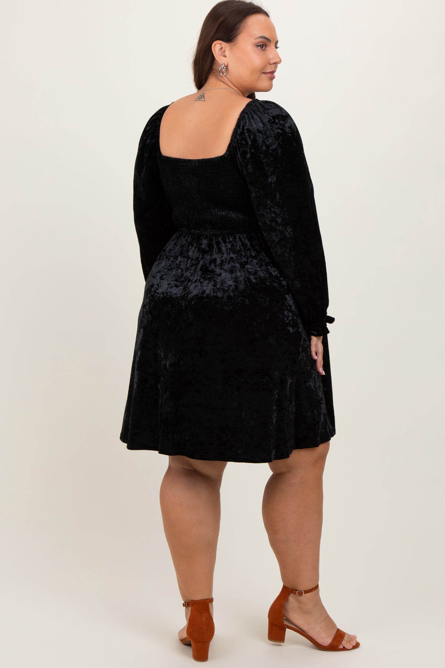 woman wearing a black velvet plus size dress with a ruched back and long sleeves, standing from the back