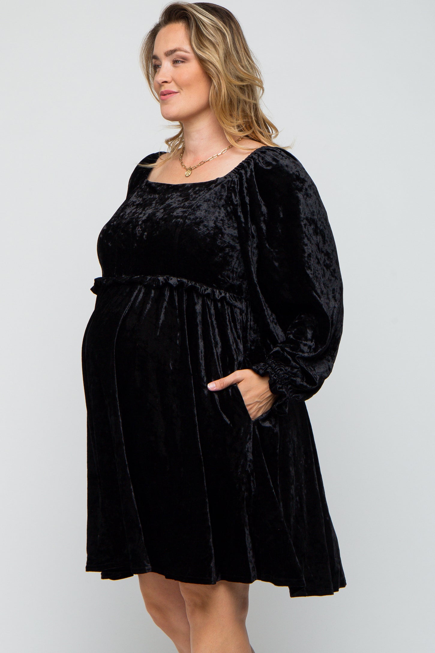 woman wearing a black velvet maternity dress with long sleeves and pockets, featuring a baby bump