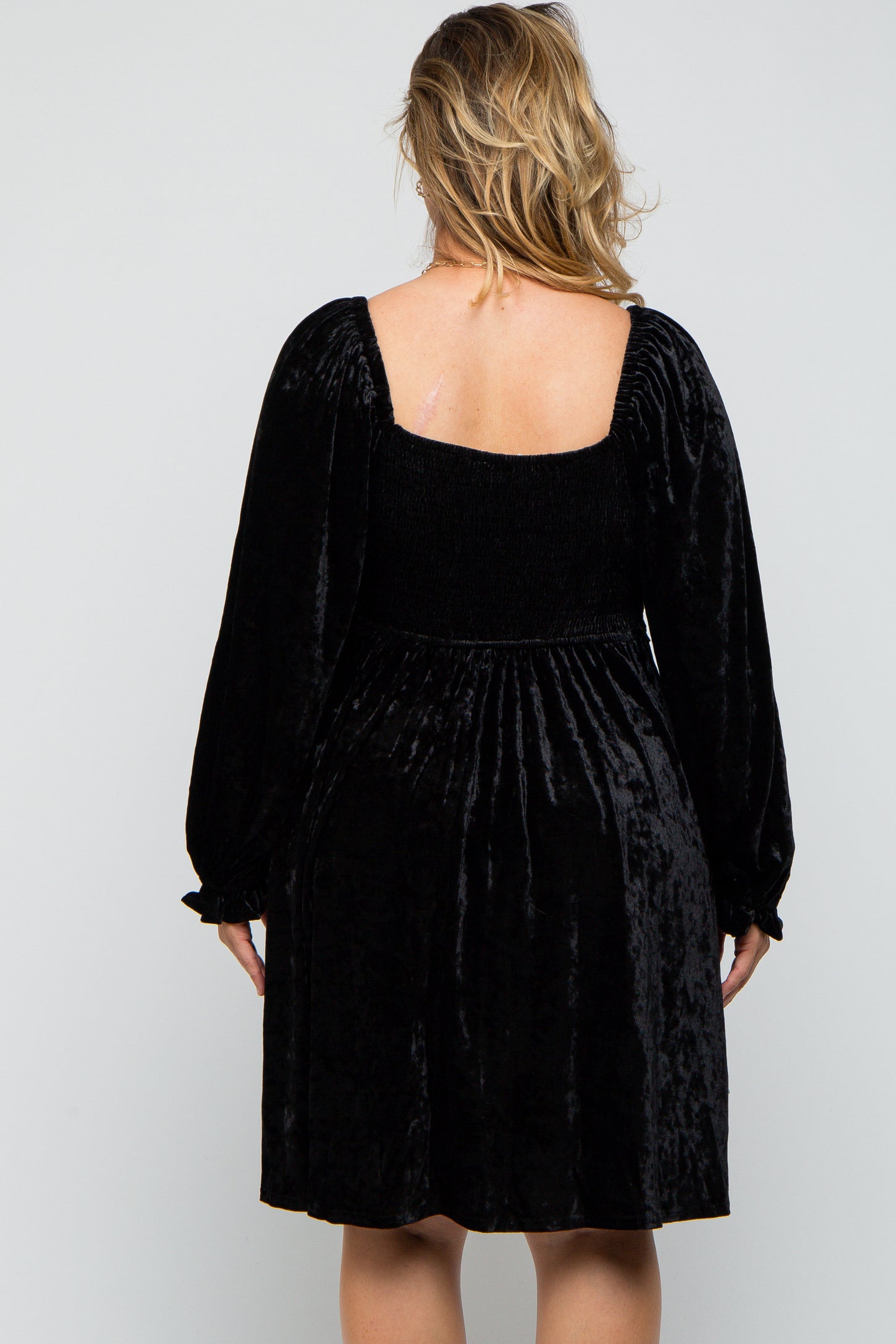 woman wearing a black velvet maternity plus dress with puff sleeves and a smocked bodice, showing her back
