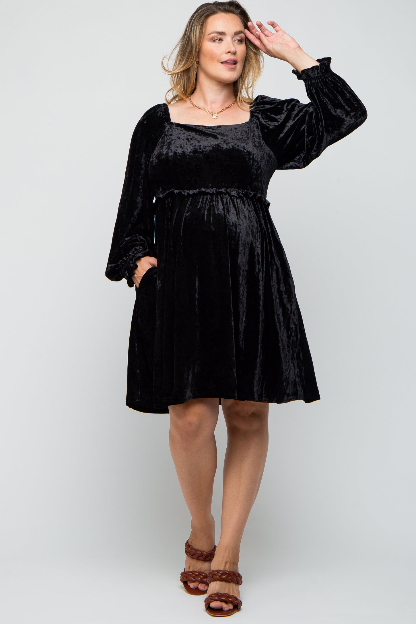 woman wearing a black velvet maternity plus dress with long sleeves and a square neckline, highlighting her baby bump