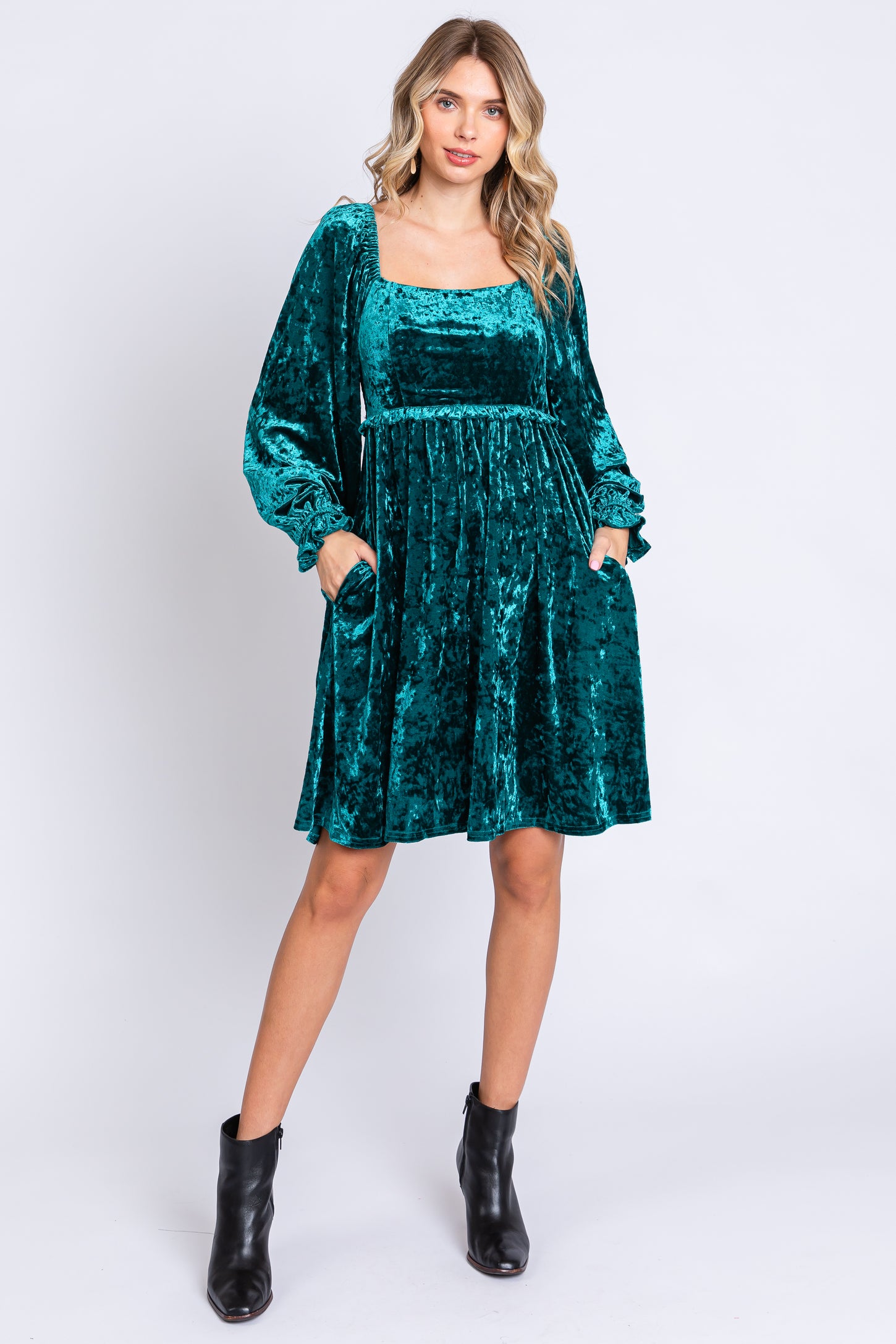 woman wearing a teal velvet long sleeve dress with a square neckline and pockets