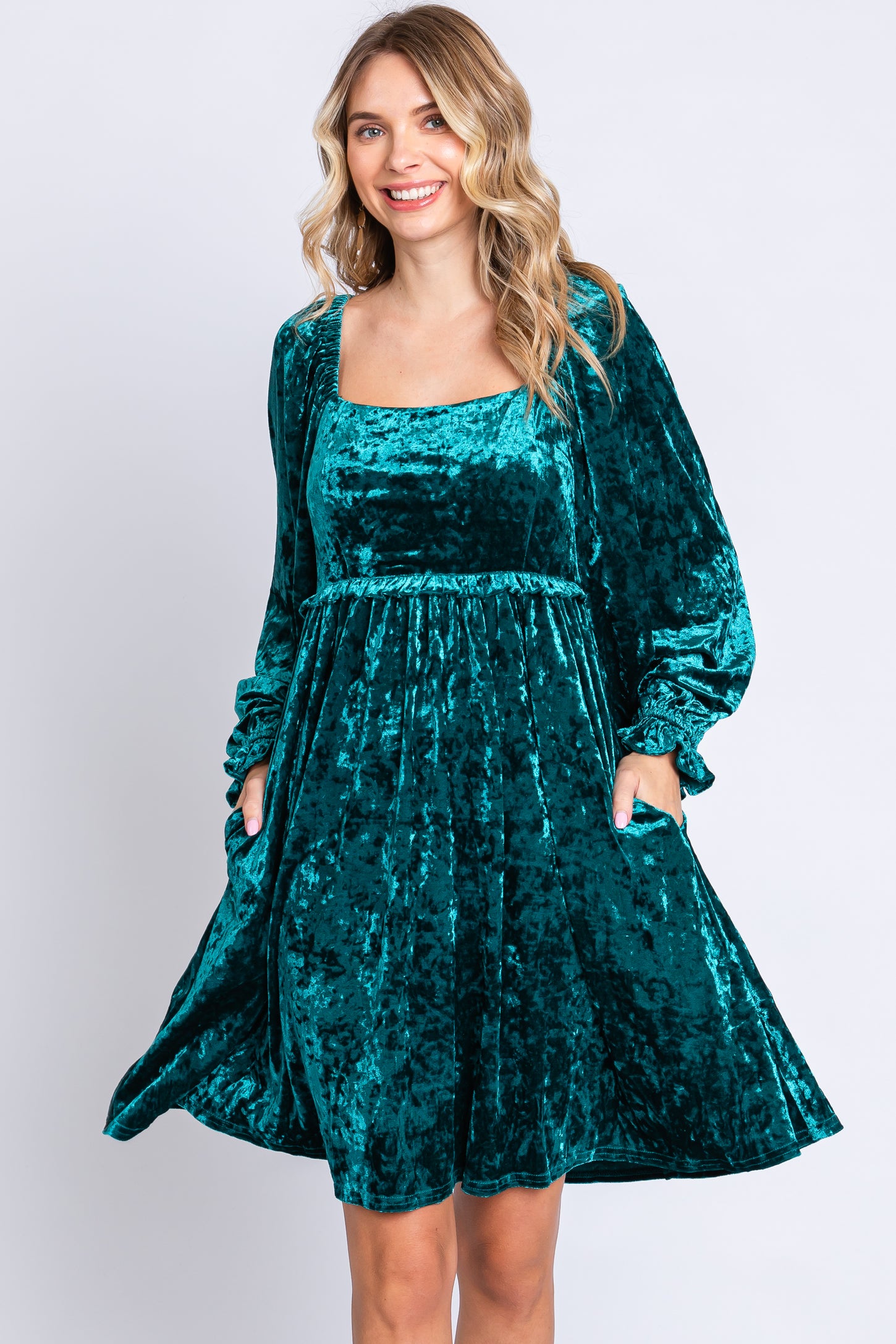 woman wearing a teal velvet long sleeve dress with a square neckline and pockets